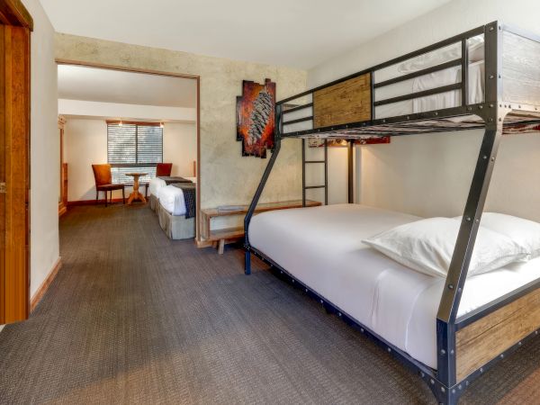 The image shows a spacious room with a bunk bed in the foreground and two single beds in the background, separated by a partially open wall partition.