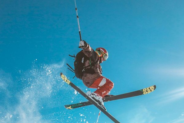 An individual is performing an airborne skiing trick above a snowy slope under a clear blue sky.