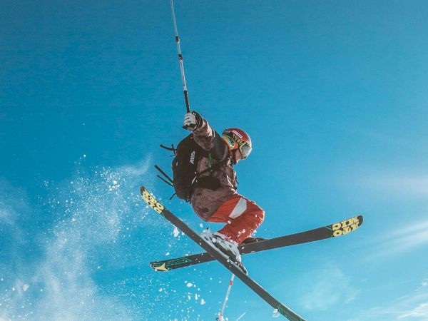 An individual is performing an airborne skiing trick above a snowy slope under a clear blue sky.