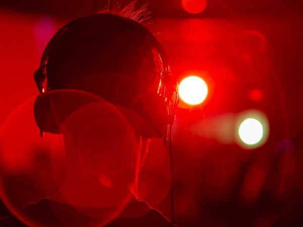A person wearing headphones is shown from the back, bathed in red lighting, with blurred bright lights in the background.