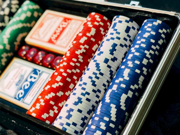 The image shows a poker set with green, red, and blue poker chips, two decks of cards, and red dice inside a case, ready for gameplay.