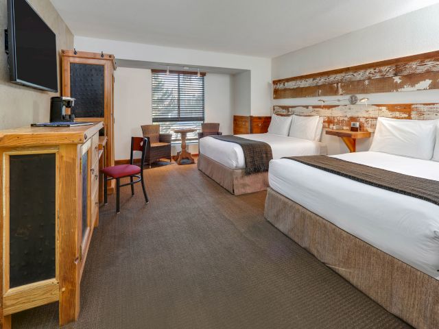 A hotel room with two beds, a TV, a table, and chairs.