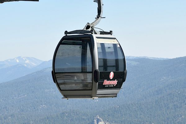 A gondola lift suspended over a mountainous landscape with trees, under a clear blue sky.